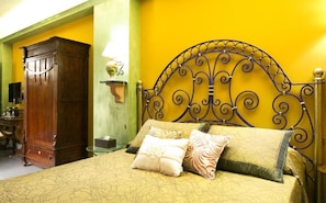Uma cama com cabeceira de metal, guarda-roupa de madeira e mesa de cabeceira com abajur.
