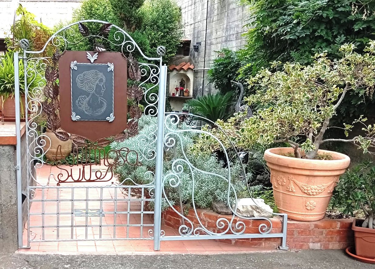 Un portail en fer forgé orné d’une plaque, des plantes en pot et un mur de briques.
