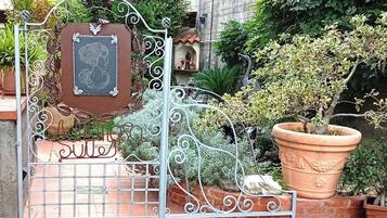 Un portail en fer forgé orné d’une plaque, des plantes en pot et un mur de briques.
