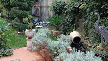 En gårdhave med fliset gulv, krukker med planter, en statue og en fugleskulptur.