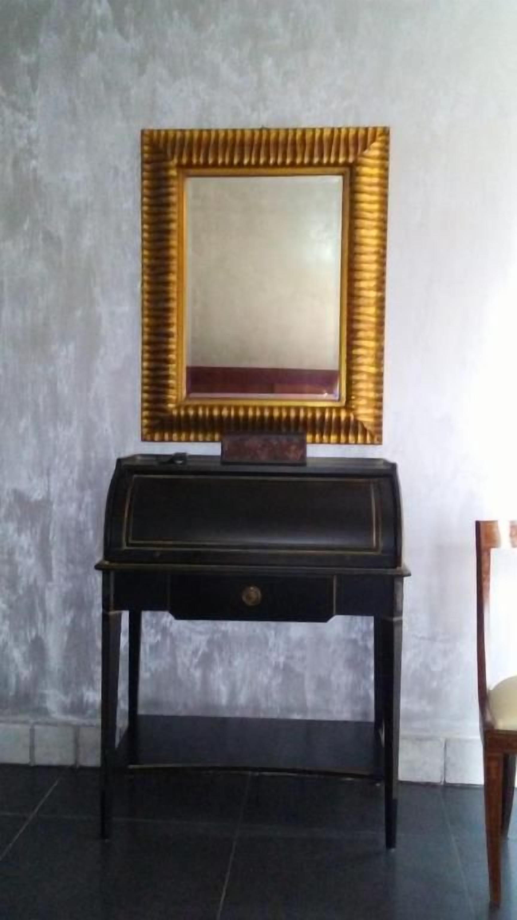 A room with a dark wooden desk, a gold-framed mirror, and a chair.