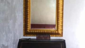 A room with a dark wooden desk, a gold-framed mirror, and a chair.