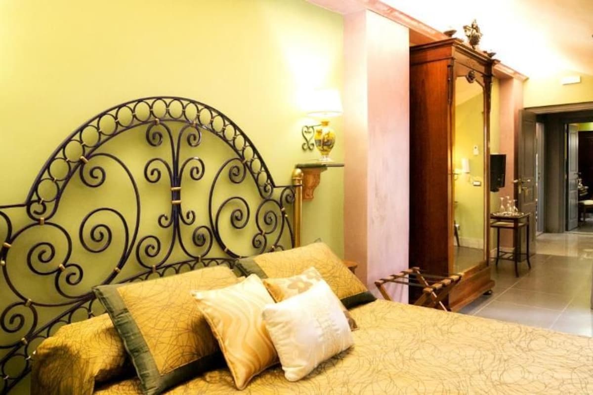Uma cama com cabeceira de metal, duas luminárias de cabeceira e uma mesinha de madeira.
