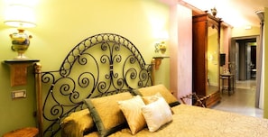 Uma cama com cabeceira de metal, duas luminárias de cabeceira e uma mesinha de madeira.