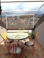 Une terrasse avec une table et des chaises, offrant une vue sur une ville pittoresque nichée sur une colline.