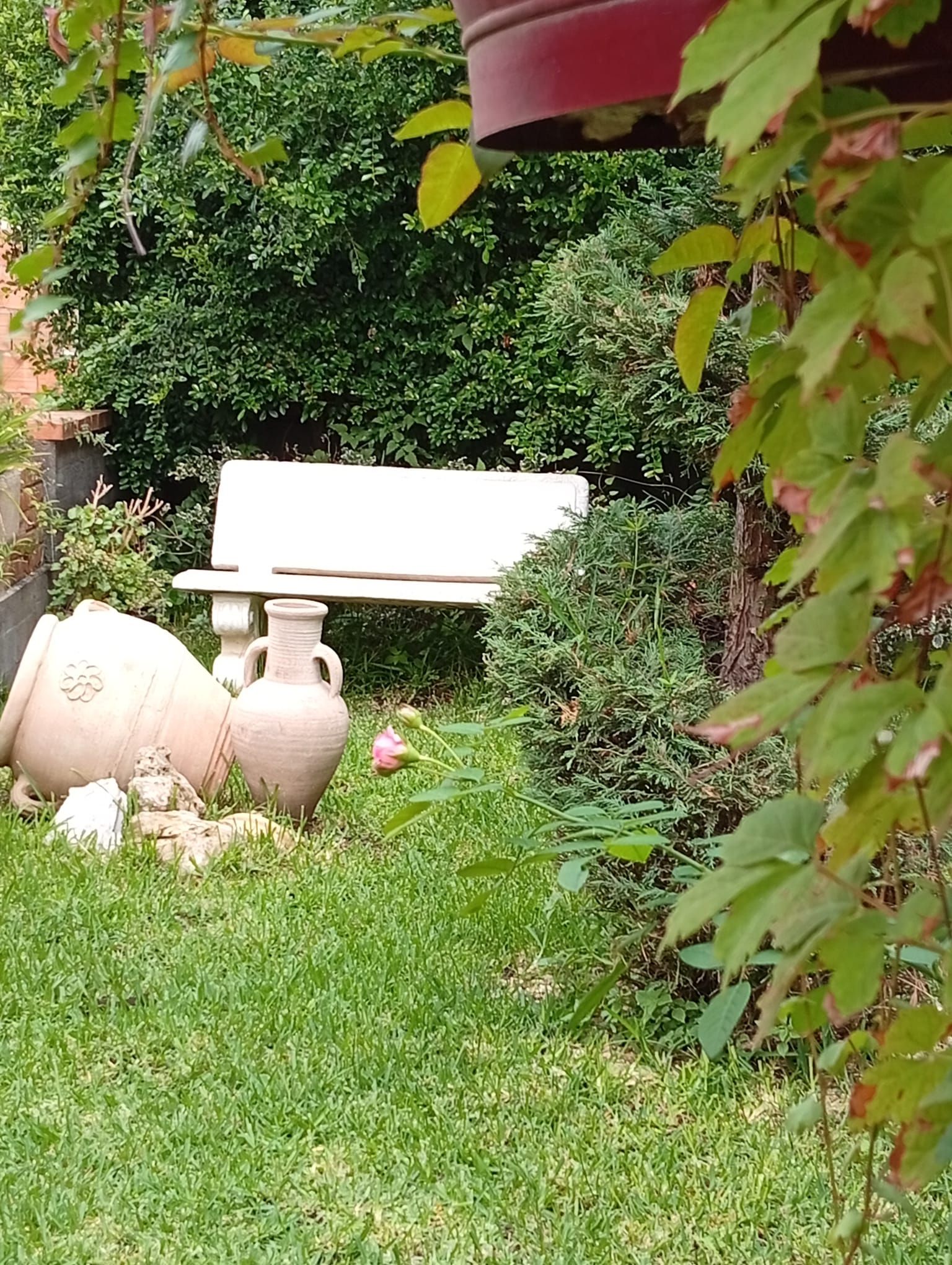 Un jardín con un jarro blanco y una jardinera de piedra.