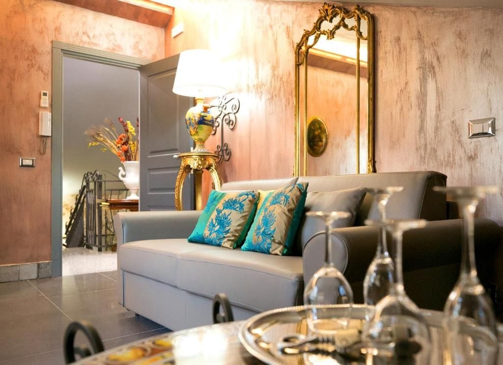 Una sala de estar con sofá, lámpara, espejo y una mesa de comedor con copas de vino.