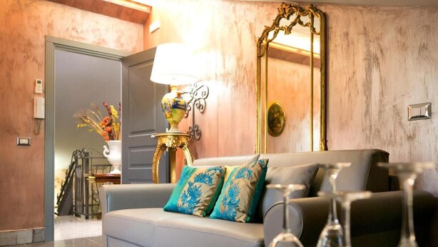 A living room with a sofa, a lamp, a mirror, and a dining table with wine glasses. - Animosa Suite (Castiglione di Sicilia)