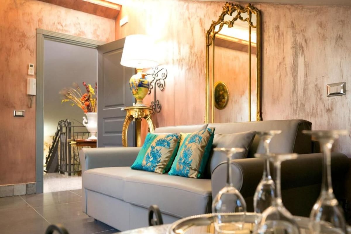 Sala de estar com sofá, luminária, espelho e mesa de jantar com taças de vinho.