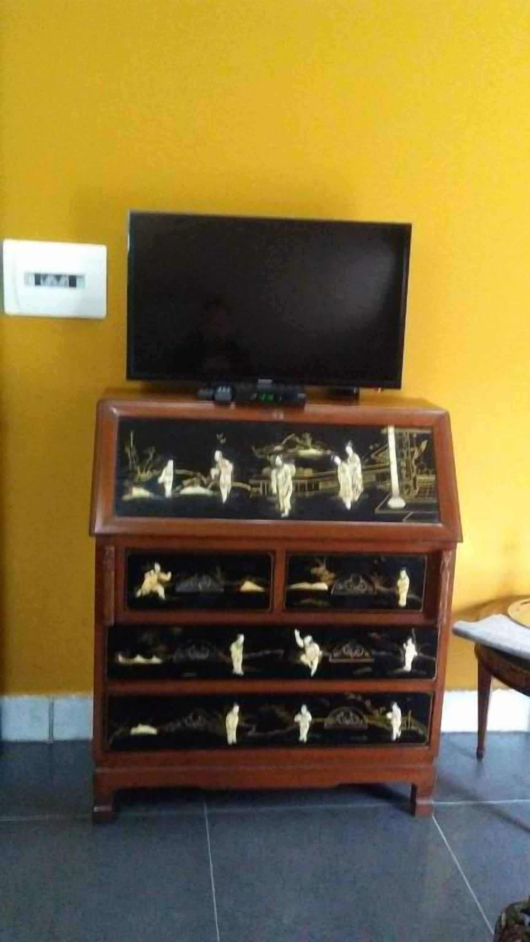Een houten kast met meerdere lades tegen een gele muur, een televisie erboven bevestigd en een betegelde vloer.