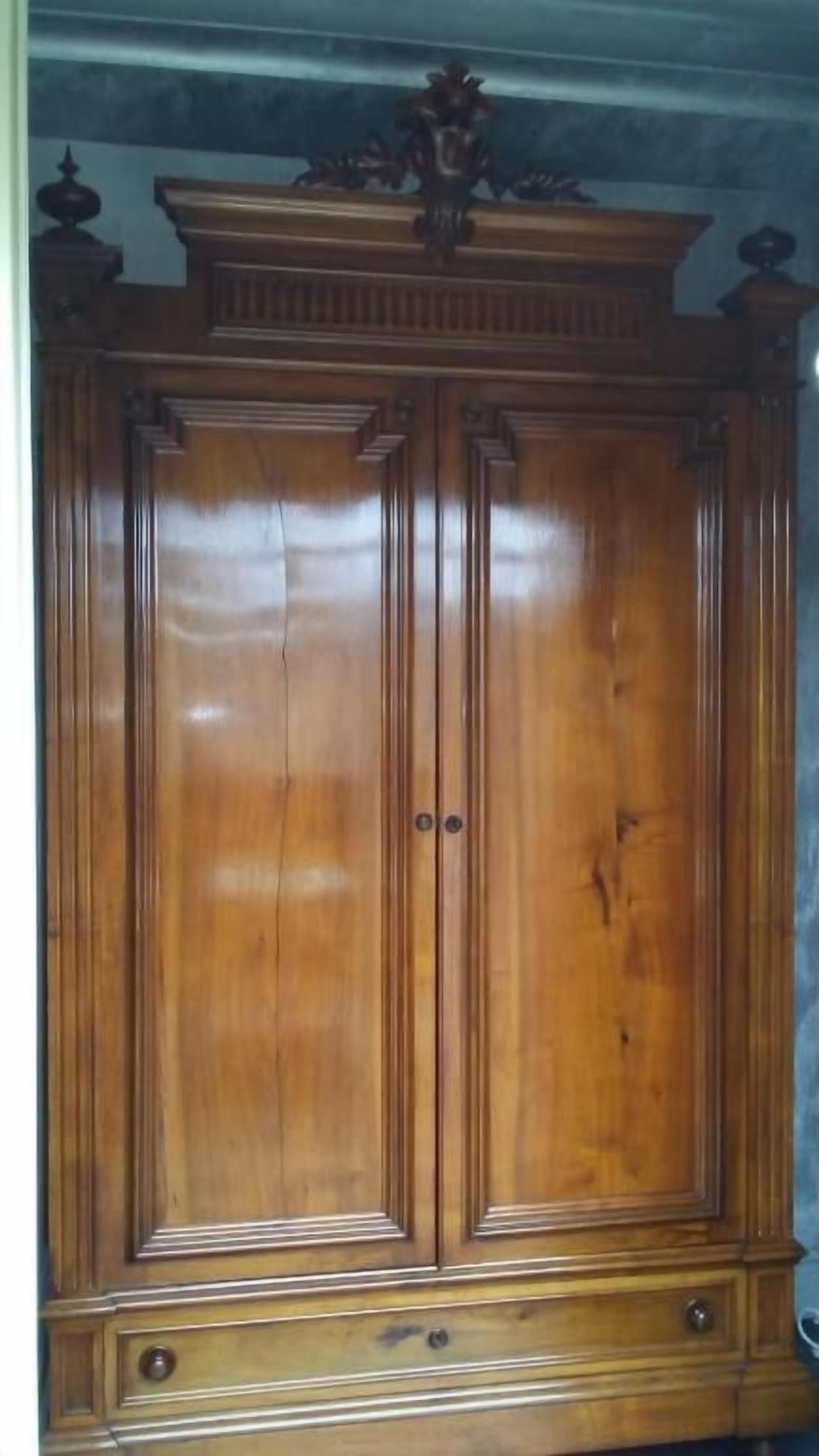 Une grande armoire en bois à deux portes, avec un dessus décoratif et une base dotée de poignées.
