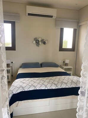 Un dormitorio con una cama, dos mesitas de noche, un equipo de aire acondicionado y una ventana.