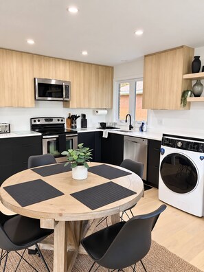 A modern kitchen with wooden cabinets, stainless steel appliances, a dining table with black placemats, and a washing machine. - Modern 3BR Home Near CHEO & General Hospital -NO PETS (Ottawa)