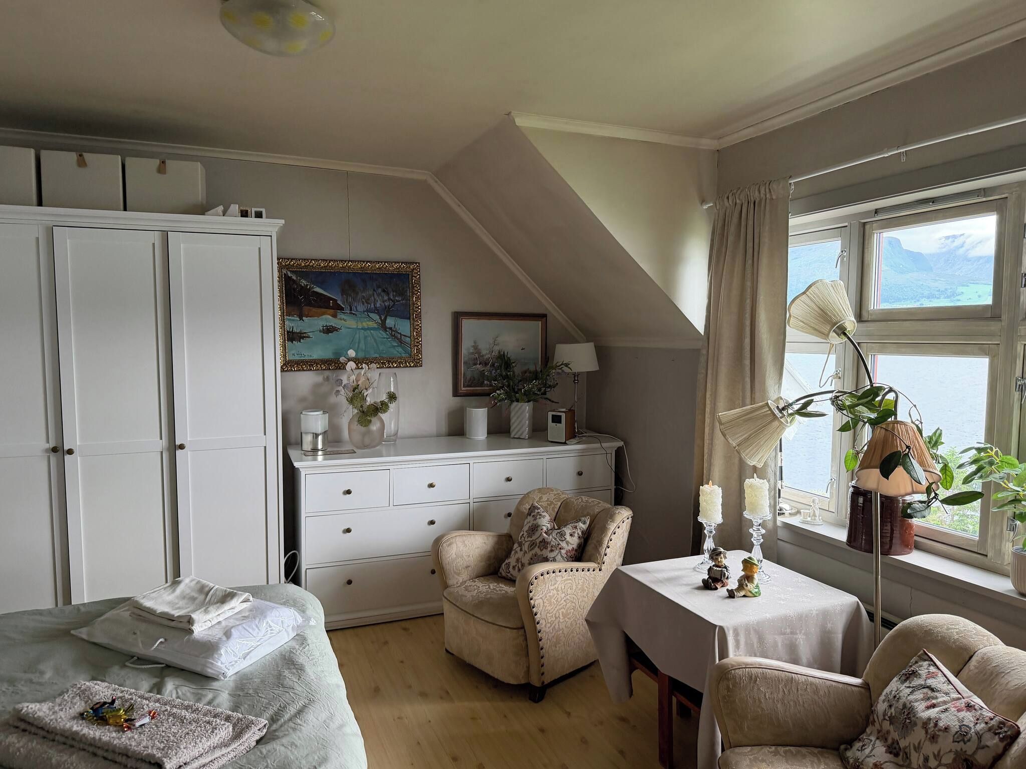 Une chambre avec un lit, un bureau, une chaise, une armoire et une fenêtre donnant sur un beau paysage.