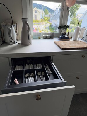 A kitchen counter with a kettle, a cutting board, and a window with a view of houses.