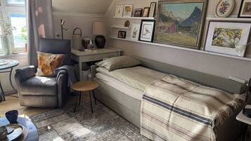 A compact room with a single bed, a chair, a small table, and a desk with a lamp.