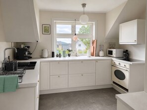 A modern kitchen with white cabinetry, a large window, and a view of houses outside. - Central 2-Bedroom Sea View Apartment (Volda)