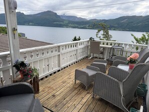 A deck with wicker furniture and a view of a lake and mountains.
