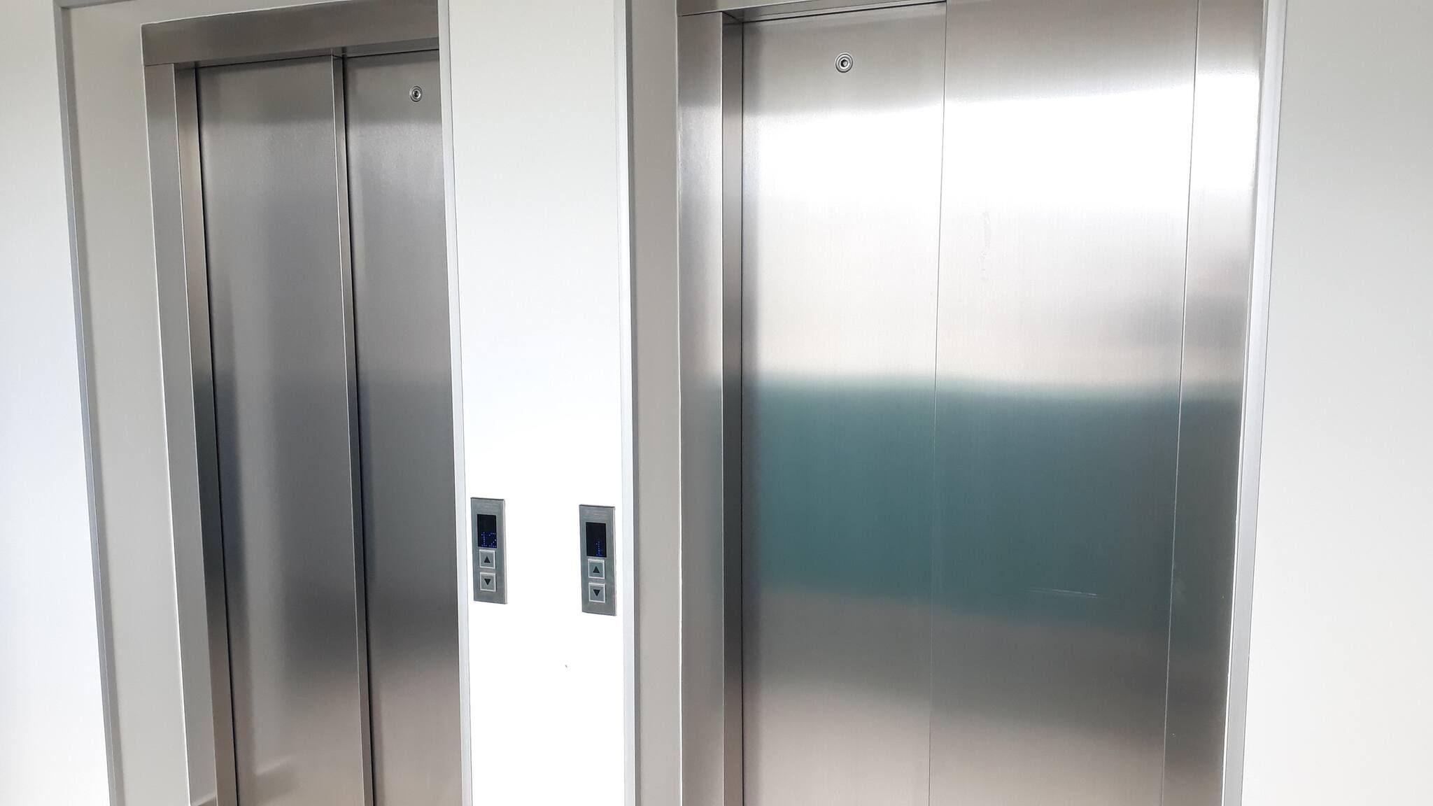 Two metallic elevator doors with control panels.