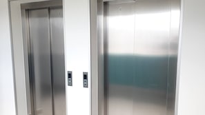 Dos puertas metálicas de ascensor con paneles de control.