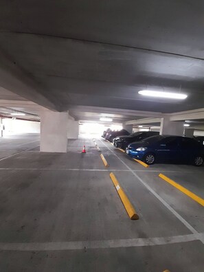 An underground parking garage with concrete pillars, fluorescent lighting, and marked parking spaces.