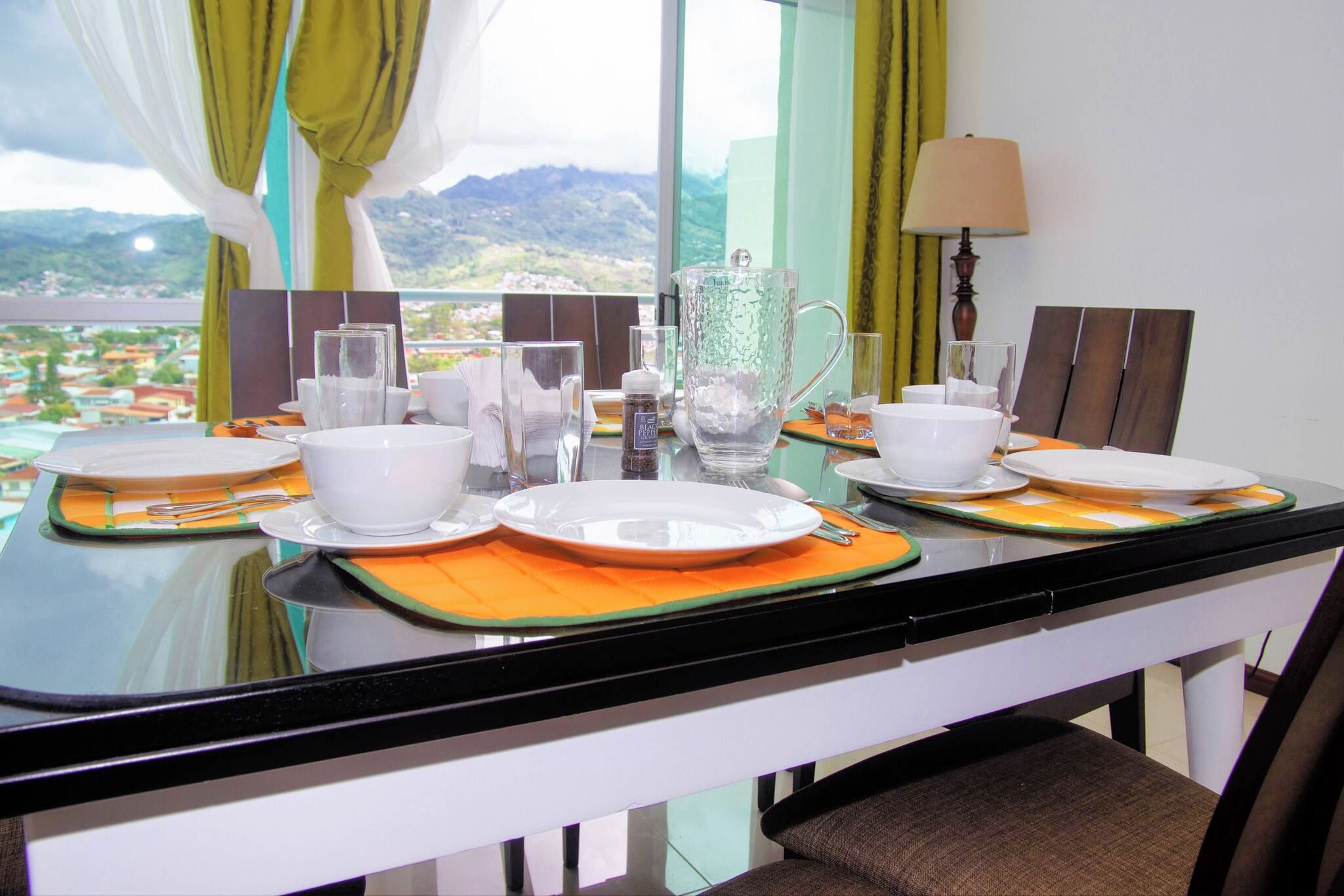 A dining table set with white plates, bowls, and glasses, with a view of mountains in the background.