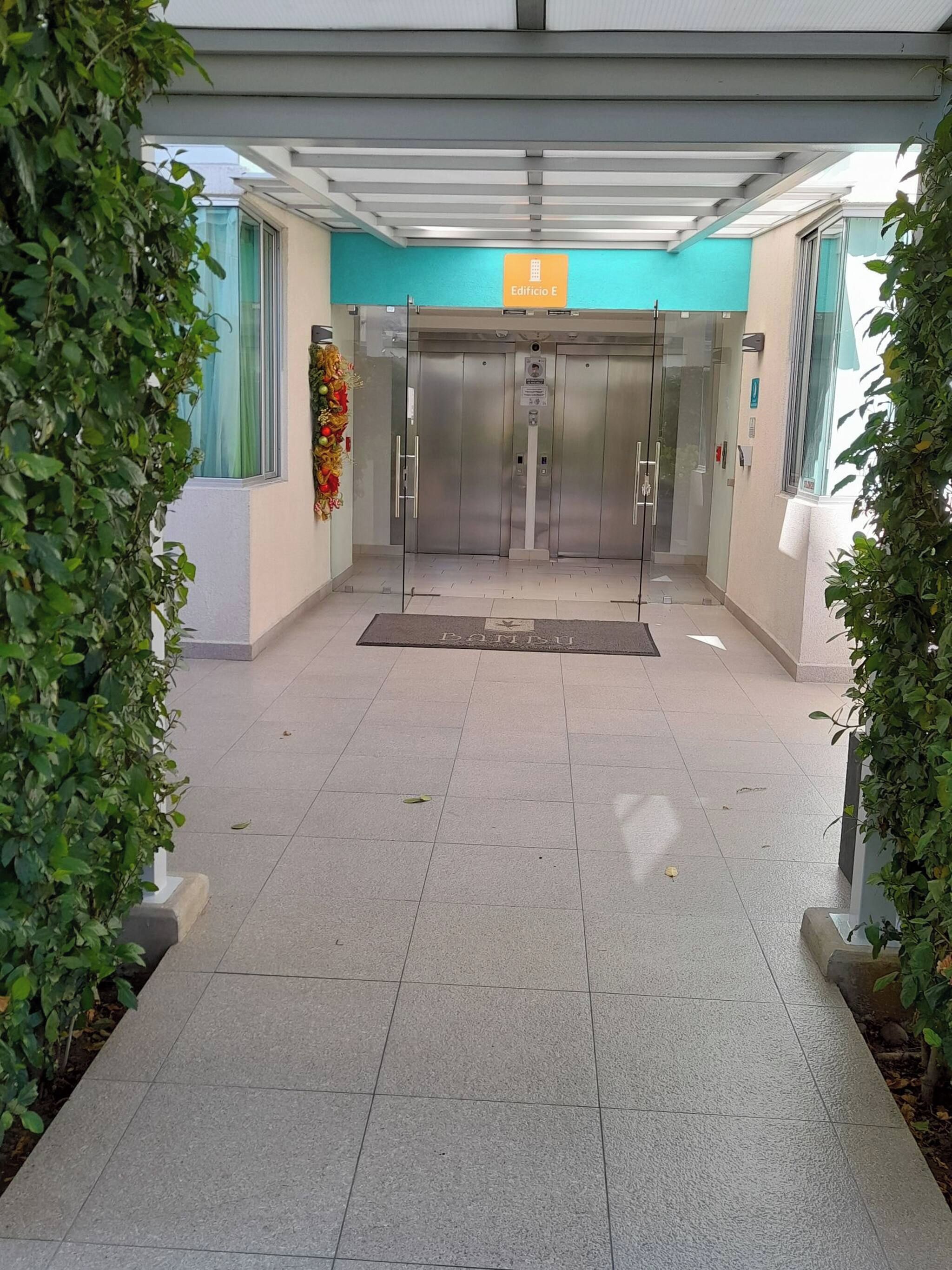 A building entrance with a sign for 'Edificio E,' a glass elevator, and a tiled floor.