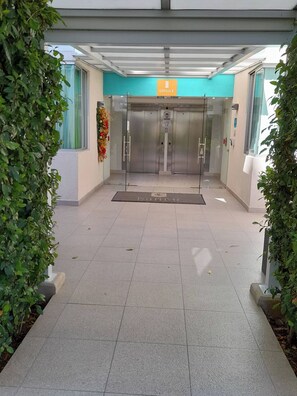 Entrada de un edificio con un letrero que dice 'Edificio E', un ascensor de vidrio y un piso de baldosas.