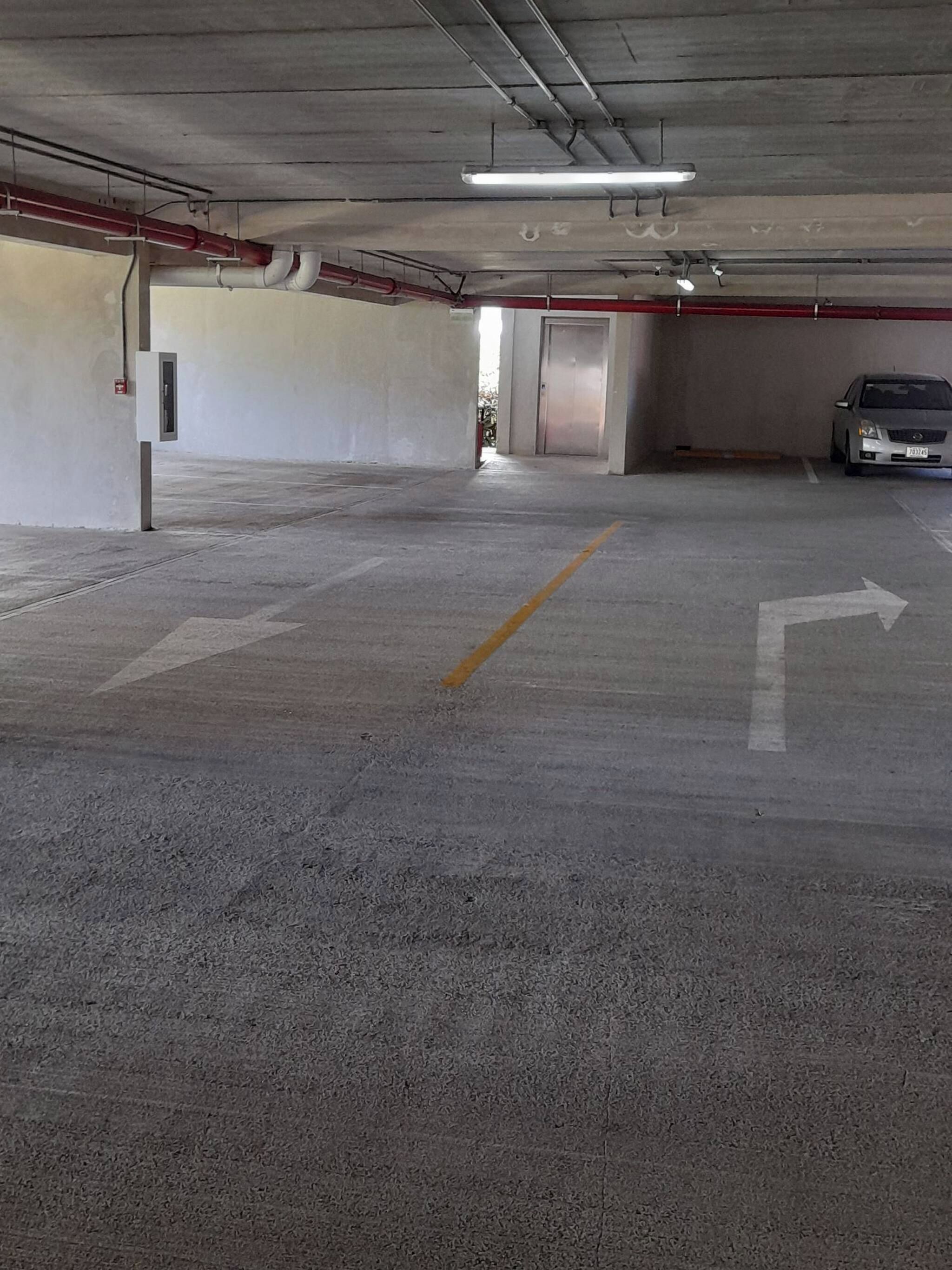 An empty parking garage with concrete floors, directional arrows, and a car parked in the distance.