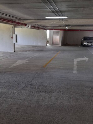 Un estacionamiento vacío con pisos de concreto, flechas direccionales y un coche aparcado a lo lejos.
