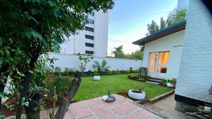Un edificio moderno con un patio empedrado, rodeado de follaje y una pared blanca.