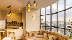 Un espacio habitable moderno con un sofá curvo, una mesa de comedor y vistas a la ciudad a través de amplios ventanales.