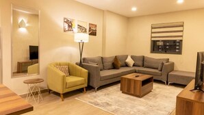 Una sala de estar con sofá, sillón amarillo, mesa de centro, televisor y lámpara.