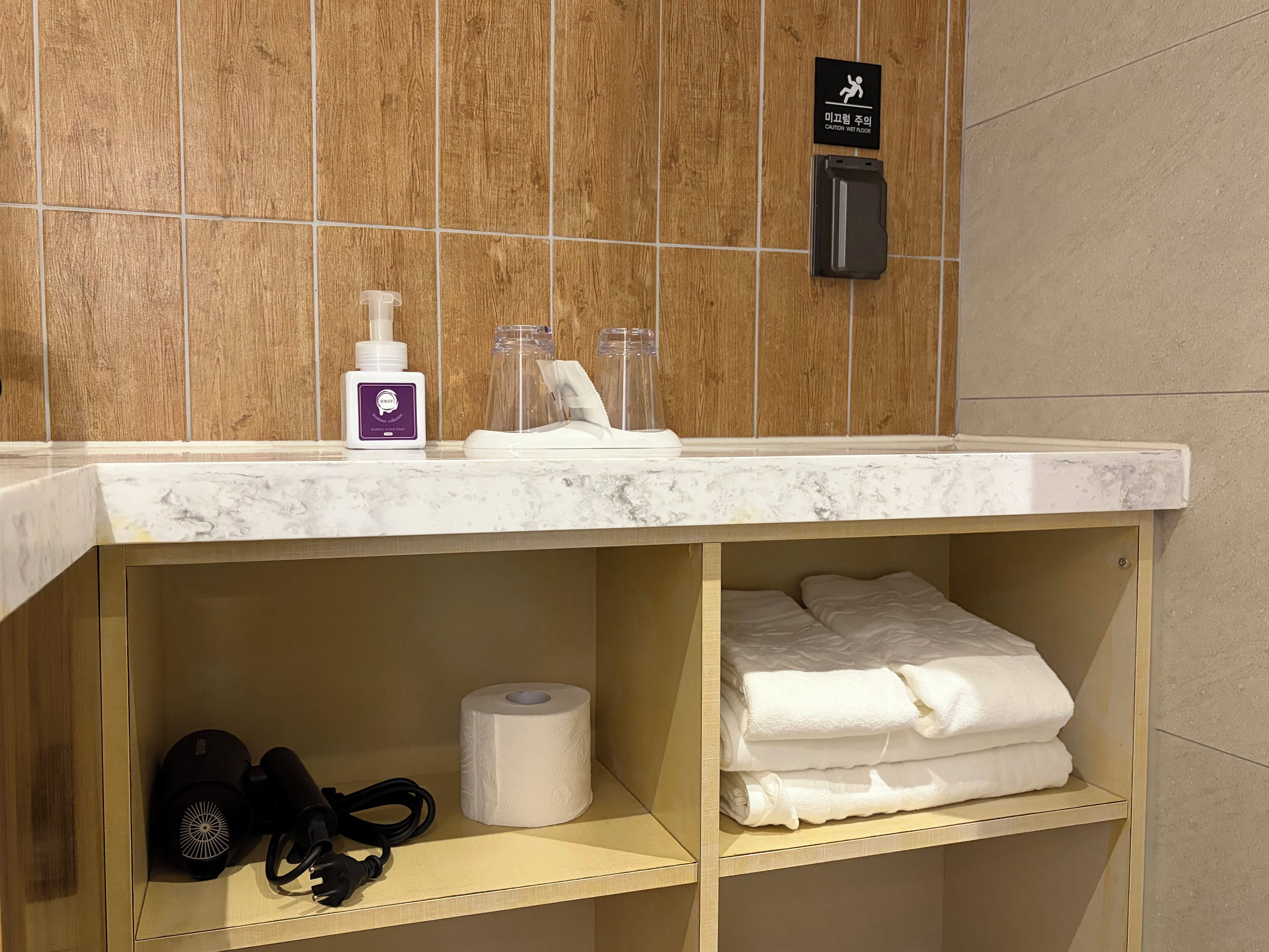 Un baño con lavamanos de mármol, un secador de manos, una botella de loción y un perchero para toallas.