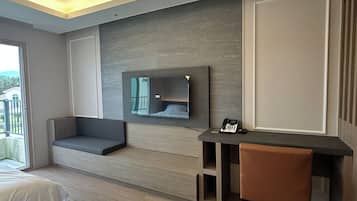 Ett modernt hotellrum med en stor säng, en sittgrupp, ett skrivbord med telefon och en tv som är monterad på väggen.