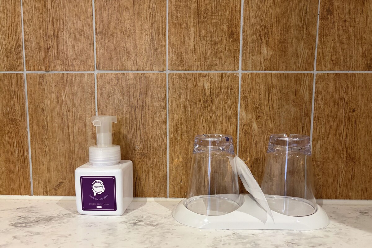 Un baño con pared de madera, una botella de jabón para manos y dos recipientes de vidrio sobre una encimera de mármol.