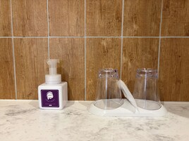 Un baño con pared de madera, una botella de jabón para manos y dos recipientes de vidrio sobre una encimera de mármol.