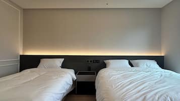 Une chambre d’hôtel avec deux lits simples, une table de chevet et un luminaire au plafond.
