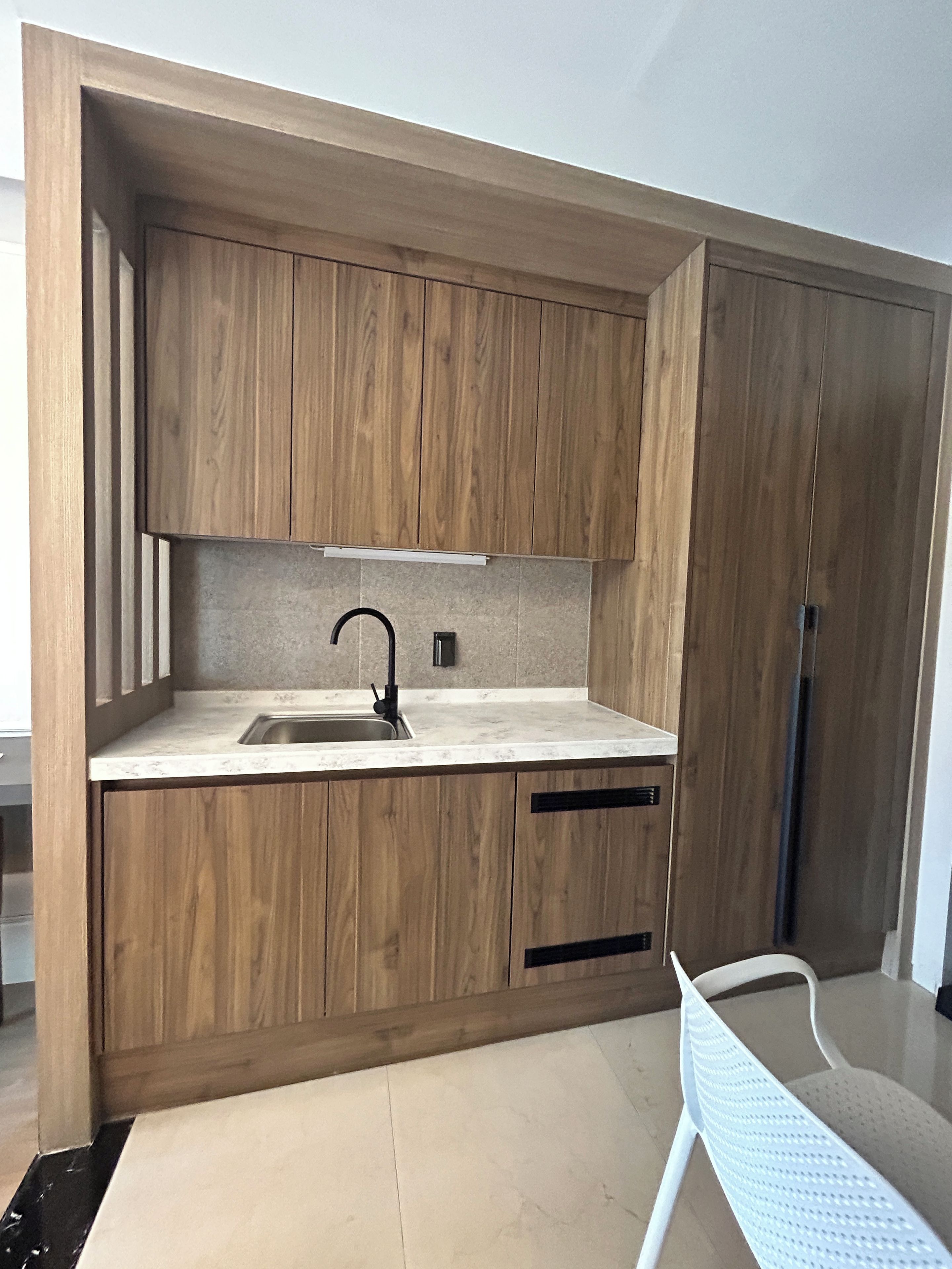 Una cocina moderna con armarios de madera, un lavamanos de acero inoxidable y una silla blanca.