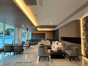 A modern hotel lobby with a seating area, a fireplace, and large windows offering a view of the outside.