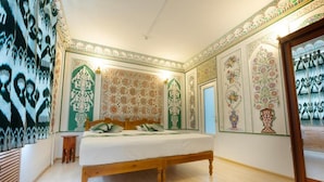 A bedroom with a wooden bed, patterned walls, and a small wooden stool. - Ismat Premium Guest House Bukhara (Bukhara)