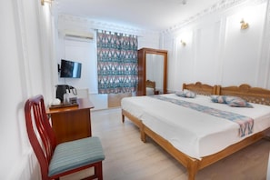 Un dormitorio con una cama de madera, un escritorio, una silla, un televisor y una cortina estampada.