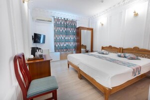 Un dormitorio con una cama de madera, un escritorio, una silla, un televisor y una cortina estampada.