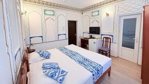 Quarto de hotel com cama, escrivaninha, cadeira e televisão.