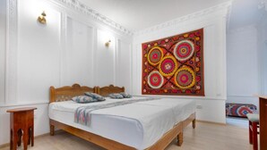 A bedroom with a wooden bed, a colorful tapestry on the wall, and a small wooden nightstand. - Ismat Premium Guest House Bukhara (Bukhara)