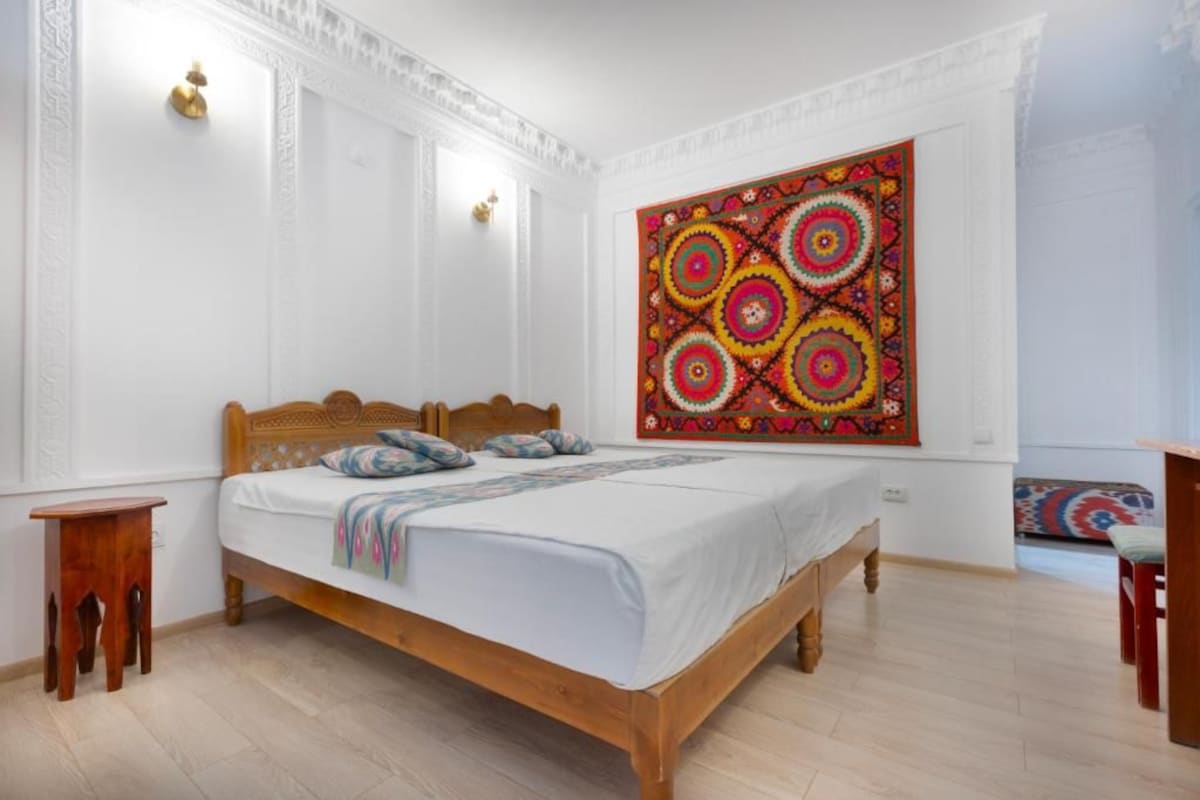 Un dormitorio con cama de madera, un tapiz de colores en la pared y una mesita de noche de madera.
