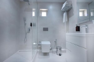 Un baño moderno con cabina de ducha de vidrio, inodoro blanco, lavabo con espejo y perchero para toallas.