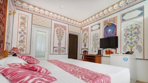 Quarto de hotel com uma cama grande, televisão e painéis decorativos na parede.