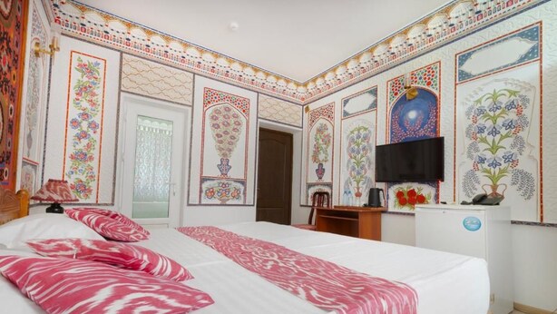 A hotel room with a large bed, a television, and decorative wall panels. - Ismat Premium Guest House Bukhara (Bukhara)