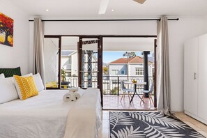 Una habitación de hotel con cama, un balcón con mesa y sillas, y vistas a edificios.